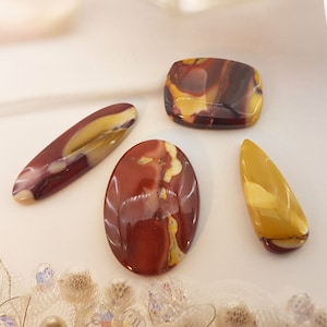 May include: Four polished, multi-colored, oval-shaped stones with red, yellow, and white patterns. The stones are arranged on a white surface.
