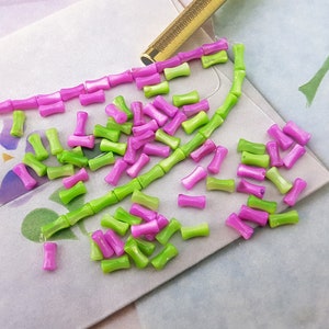 May include: A collection of small, green and pink, glass beads. The beads are shaped like short, rounded cylinders.