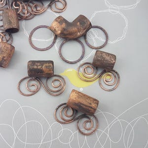 Op de afbeelding: Set van vijf koperen haar kralen met een verweerde afwerking. Elke kraal heeft een decoratief draadontwerp met een swirl-patroon.