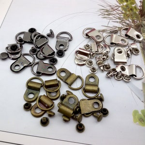 May include: Assortment of metal shoe eyelets and rivets in silver, black, and bronze. The eyelets are D-shaped and have a loop for attaching laces or straps. The rivets are small and have a flat head.