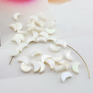 May include: A collection of white iridescent half-moon shaped ceramic tiles. The tiles are scattered on a white surface.