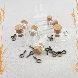 May include: A selection of small, clear glass bottles with cork stoppers and bronze-coloured screw eye pins. The bottles are cylindrical and empty, suitable for crafts. The corks are a light brown colour.