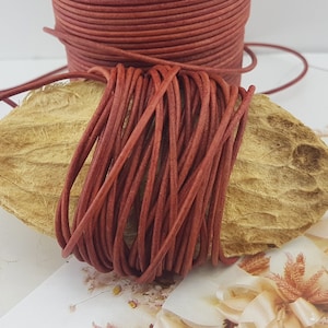 Puede incluir: Primer plano de un carrete de cordón de cuero rojo. El cordón está enrollado firmemente alrededor del carrete y está listo para ser utilizado en proyectos de artesanía.