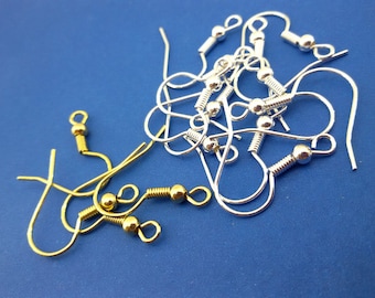 May include: A close-up of a pile of silver and gold earring hooks. The hooks are made of metal and have a small ball at the end. The hooks are on a blue background.