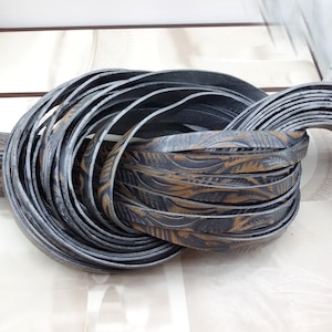 Puede incluir: Primer plano de un conjunto de cordón de cuero negro y marrón con un patrón decorativo. El cordón está enrollado y retorcido.