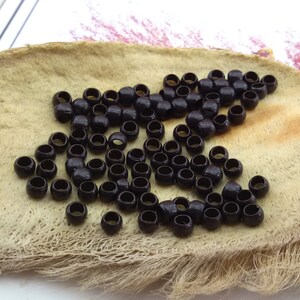 May include: A close-up of a pile of dark brown beads. The beads are round and have a smooth, glossy finish. They are arranged in a random pattern on a light brown surface.