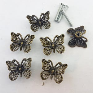 Può includere: Pomelli per mobili a forma di farfalla color bronzo, con dettagli intricati sulle ali. Sono incluse diverse viti, che suggeriscono una facile installazione. Il design a farfalla aggiunge un tocco decorativo.
