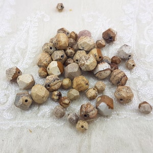Peut inclure: Un ensemble de perles de jaspe brunes, beiges et blanches avec un motif marbré. Les perles sont facettées et ont un aspect naturel et terreux.