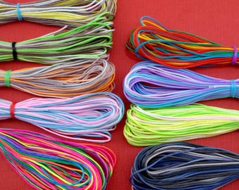 Puede incluir: Surtido de cordones de algodón encerado de colores, incluyendo rojo, verde, azul, amarillo, rosa y gris. Los cordones están dispuestos en una fila sobre una superficie roja.