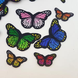 May include: Embroidered butterfly patches in various colours, including pink, green, blue, orange, and red. Each patch features detailed wing patterns and a black border. Suitable for clothing or craft projects.