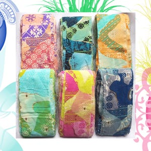 May include: Six folded fabric pieces with colorful patterns. The fabrics feature floral and geometric designs in shades of pink, blue, orange, and green. The textiles appear to be made of a lightweight material.