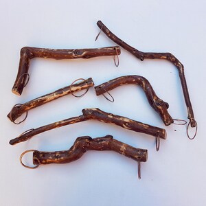 May include: Six brown wooden sticks with copper rings attached to each end. The sticks are arranged in a random pattern on a white surface.