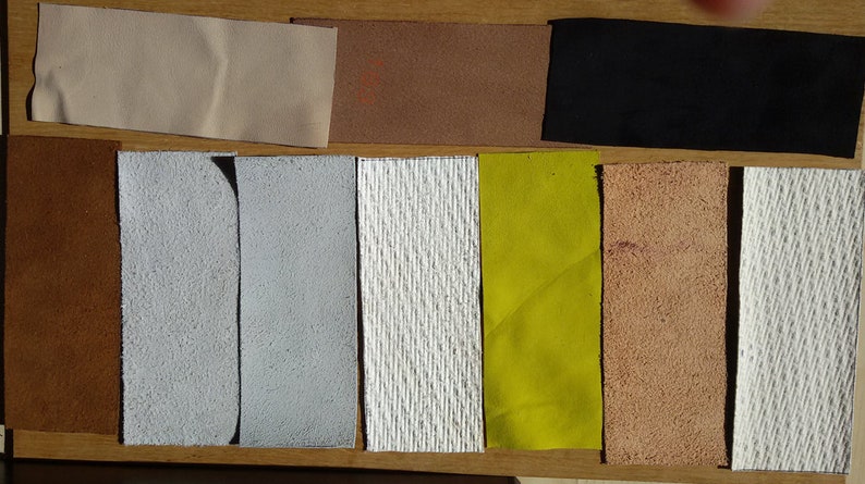 May include: A collection of ten fabric swatches in various colours and textures, including beige, brown, black, white, grey, yellow, and tan.