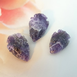 Può includere: Tre punte di freccia di ametista viola con una texture ruvida e naturale.