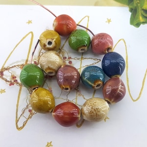 Peut inclure: Un ensemble de 12 perles en céramique de différentes couleurs, notamment vert, bleu, marron, jaune et rouge. Les perles sont de forme ovale et ont une surface mouchetée ou texturée.