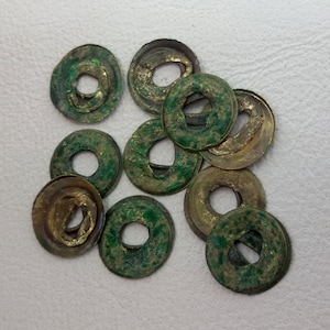 Puede incluir: Una colección de diez monedas redondas de cobre con un agujero en el centro. Las monedas son de color verde y dorado y tienen un aspecto desgastado y antiguo.