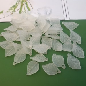 Könnte beinhalten: Eine Sammlung durchscheinender weißer Plastikblätter mit einer strukturierten Oberfläche. Die Blätter sind in Form eines einfachen Blattes mit einer spitzen Spitze und einer abgerundeten Basis geformt. Jedes Blatt hat ein kleines Loch oben zum Aufziehen.
