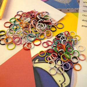 May include: A large pile of colorful metal rings, some are white, some are black, and many are bright colors like red, orange, yellow, green, blue, and purple.