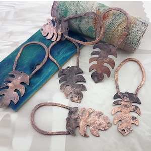 May include: A set of seven copper-toned leaf-shaped pendants with intricate cutouts. The pendants are strung on a wire and have a rustic, handmade look.