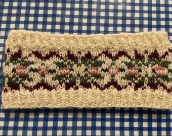 May include: A white knitted headband with a burgundy, green, and pink patterned design.