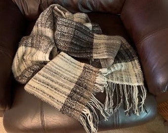 May include: A soft, woven scarf with a black and white checkered pattern and fringe. The scarf is folded and draped on a brown leather couch.