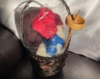May include: A brown wicker basket with a handle, containing a plastic bag of colorful wool yarn and a wooden spinning wheel.
