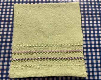 May include: A light green woven pillow with a decorative border of purple and green flowers.