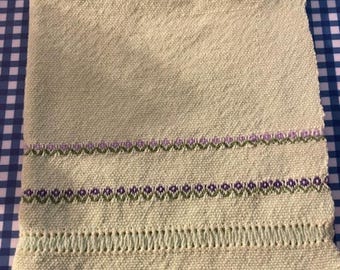May include: A light green kitchen towel with a decorative embroidered border in shades of green and purple.
