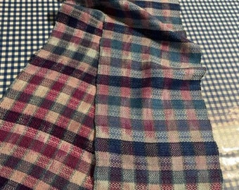 May include: A woven scarf with a pink, blue, and white plaid pattern. The scarf has fringe on both ends.