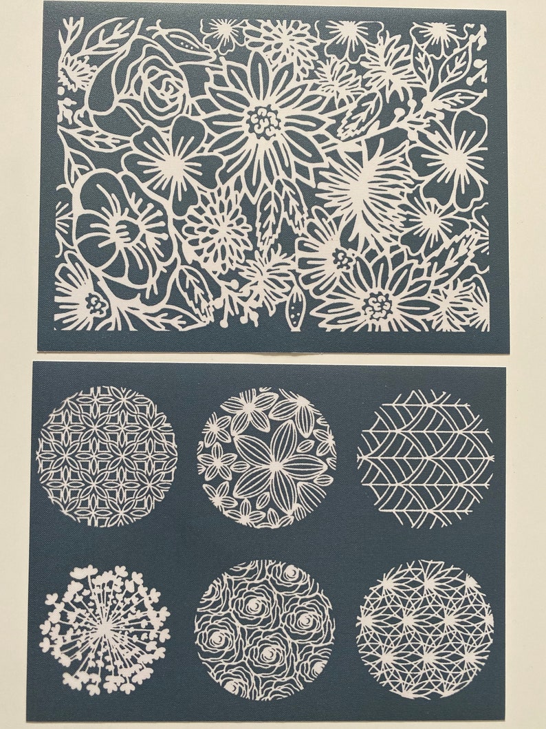 May include: Two sheets of white vinyl stencils with floral and geometric designs. The top sheet features a large floral pattern with various flower shapes and sizes. The bottom sheet has six circular stencils with different patterns, including a floral design, a geometric pattern, and a design resembling a starburst.
