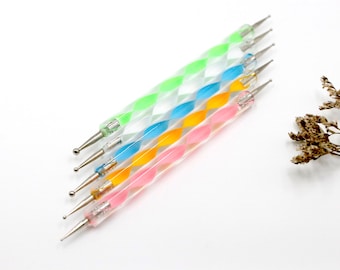 Può includere: Set di sei strumenti per nail art a punti di colori diversi con punte di diverse dimensioni. Gli strumenti hanno un manico in plastica trasparente con un motivo a spirale in verde, blu, arancione e rosa.