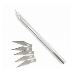 May include: A silver craft knife with a textured handle and a sharp, angled blade. Five replacement blades are included, each with a pointed tip and a small hole. The tools are set against a white background.