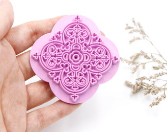 Puede incluir: Primer plano de un sello de goma rosa con un diseño floral intrincado. El sello se sostiene en una mano, y el fondo es blanco.