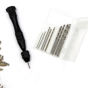 Könnte beinhalten: Eine schwarze Handbohrmaschine mit einem Satz Bohrer in einem durchsichtigen Kunststoffkoffer. Die Bohrer sind nach Größe sortiert.