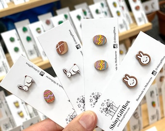 May include: Assortment of wooden earrings featuring various designs, including bunnies, Easter eggs, and a hot cross bun. The earrings are displayed on white cards with the text "ShinyGiftBox" and "Handmade in Melbourne" on them.