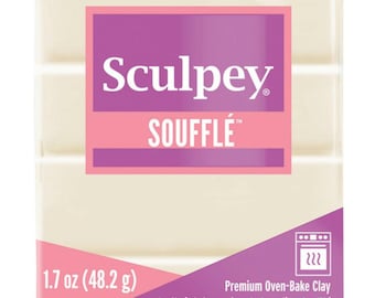 Pode incluir: Um bloco de argila para assar no forno da marca Sculpey Souffle de 1,7 onças (48,2 gramas). A argila é branca e está embalada em uma caixa rosa e branca com o nome da marca e o nome do produto impressos nela.