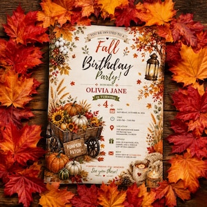 May include: A rectangular fall birthday party invitation for Olivia Jane turning 4, featuring a wooden wagon filled with pumpkins, sunflowers, and wheat, surrounded by autumn leaves, a lantern, and event details for October 26, 2024.