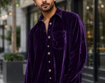 May include: A long-sleeved button-down shirt made of deep purple velvet fabric. The shirt features a classic collar, a single chest pocket on the left side, and gold-toned circular buttons running down the front placket and on the sleeve cuffs.