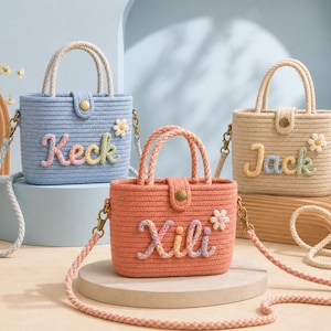 May include: Three small structured handbags made of woven rope in light blue, peach, and beige. Each bag features a top handle, a detachable shoulder strap, a gold-tone snap closure, and a small white daisy appliqué. The names Keck, Xili, and Jack are embroidered on the front of each bag in colorful, textured lettering.