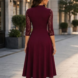 Puede incluir: Un vestido color burdeos hasta la rodilla con mangas de encaje de tres cuartos, cuello alto y un corpi&ntilde;o ajustado que se transforma en una falda acampanada. La prenda es de color s&oacute;lido con detalles de encaje floral en las mangas.