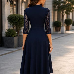 Puede incluir: Un vestido midi azul marino con mangas de encaje de tres cuartos, cuello alto y un corpi&ntilde;o ajustado que se transforma en una falda acampanada. La prenda es de color azul marino s&oacute;lido con detalles de encaje floral en las mangas.