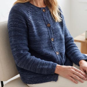 May include: A navy blue knit cardigan featuring a textured, heathered appearance with a round neckline and four brown buttons down the front. The long-sleeved garment has ribbed cuffs and a ribbed hem, showcasing a consistent knit pattern throughout.