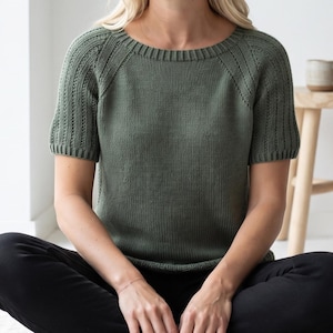May include: A short-sleeved, olive green knitted sweater featuring a round neckline and ribbed detailing along the collar, cuffs, and raglan sleeve seams. The garment is constructed with a smooth stockinette stitch body and textured ribbed sleeves.