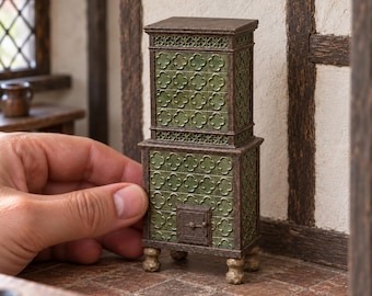May include: A miniature two-tiered stove featuring a dark brown frame and green square tiles embossed with a repeating quatrefoil pattern. The stove stands on four small, rounded feet and includes a central square door with a small metal handle.