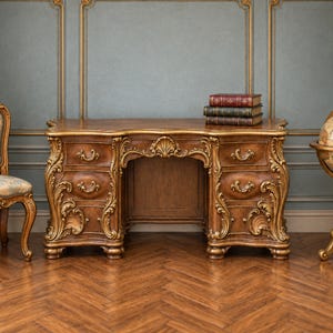 May include: A brown wooden desk featuring ornate carved scrollwork, a central shell motif, and four drawers with curved fronts and metal pulls. Three stacked books with red and green covers rest on the flat, polished surface of the desk.