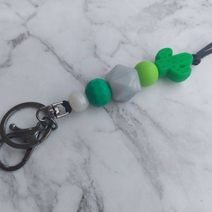 May include: A green cactus charm keyring with a silver key ring and green, white and grey beads.