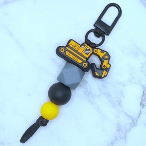 May include: A yellow and black toy excavator keychain with a gray, black, and yellow silicone bead chain.