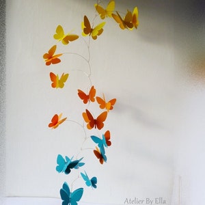 May include: A mobile with a spiral design featuring butterflies in shades of yellow, orange, and blue. The mobile is suspended from a white ceiling.