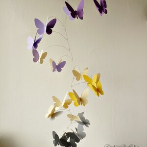 May include: A mobile with butterflies in shades of purple, yellow, and gray. The butterflies are suspended from a wire frame and hang at different levels. The mobile is a whimsical and decorative piece for a nursery or child's room.
