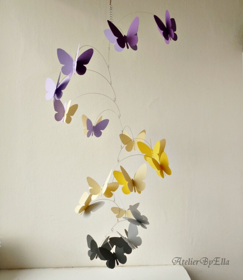 May include: A mobile with butterflies in shades of purple, yellow, and gray. The butterflies are suspended from a wire frame and hang at different levels. The mobile is a whimsical and decorative piece for a nursery or child's room.